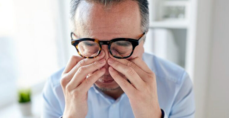 businessman in glasses rubbing eyes at office